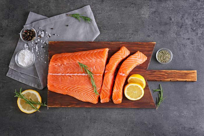 Cutting board with fresh salmon fillet and lemons on table