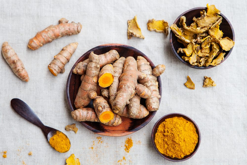 Fresh and dried turmeric roots in a wooden bowl. Grey textile background. Top view.