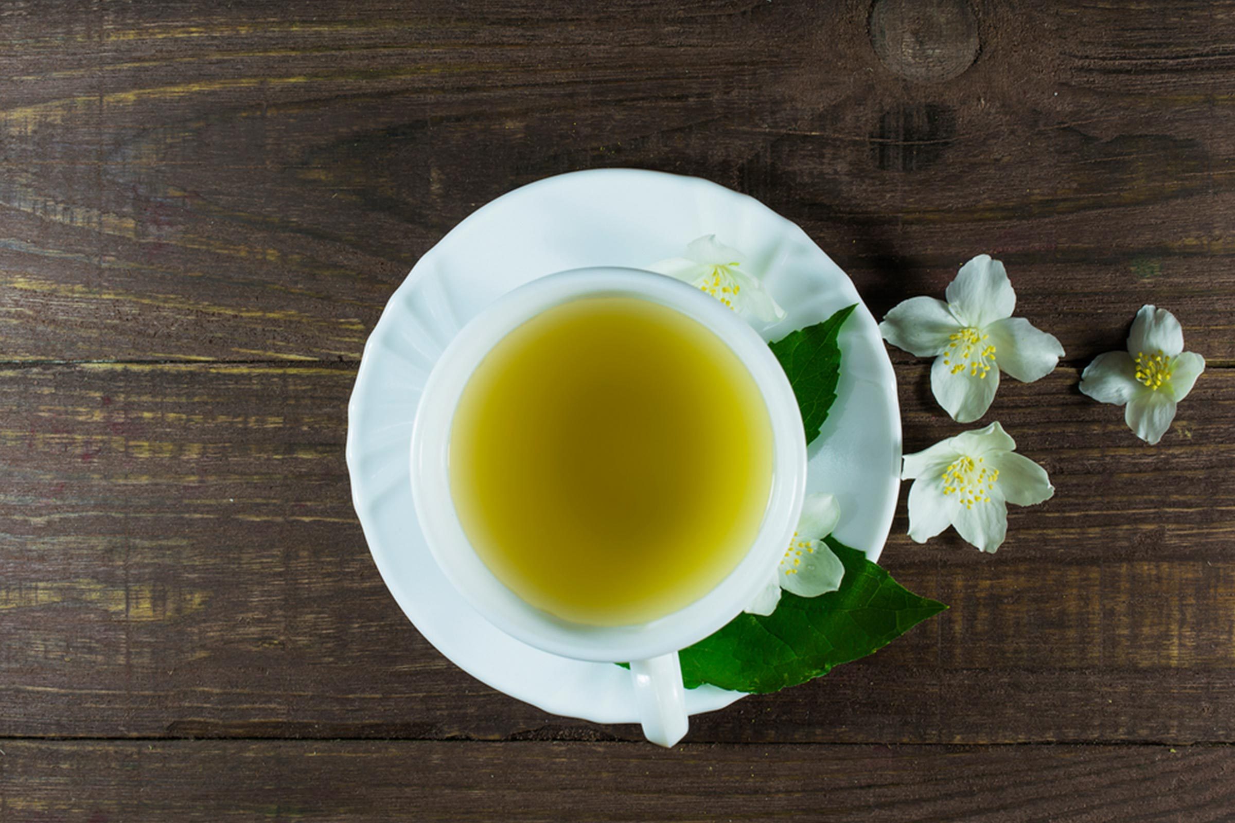 Cup of green tea on saucer with jasmine flowers