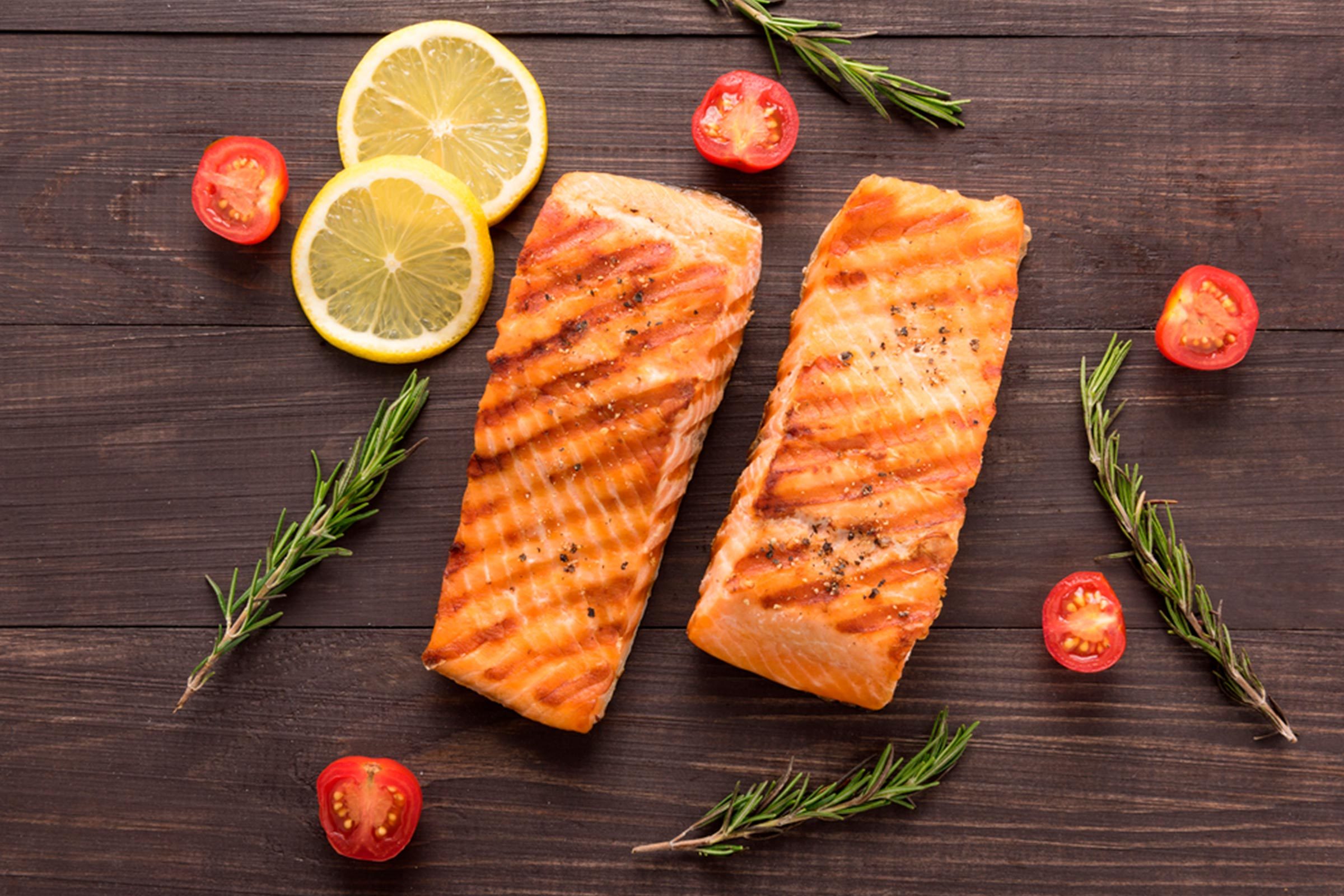 Two grilled salmon filets with rosemary, tomatoes, and lemon slices