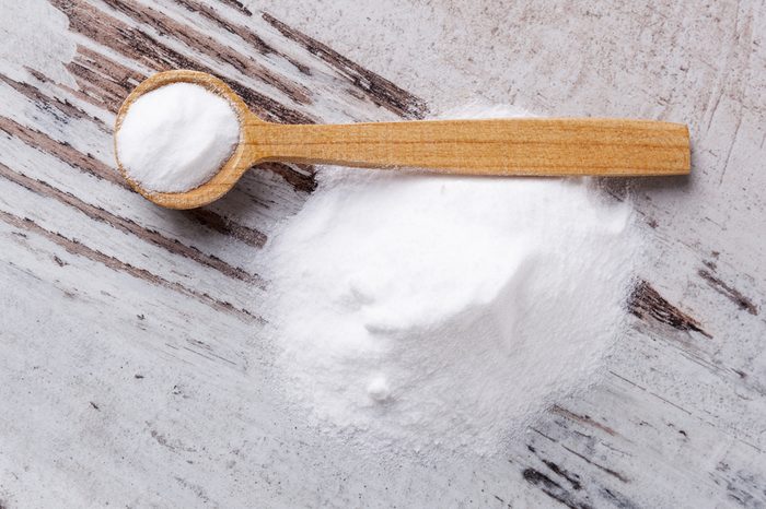 Baking soda on wooden spoon on white wooden textured background.