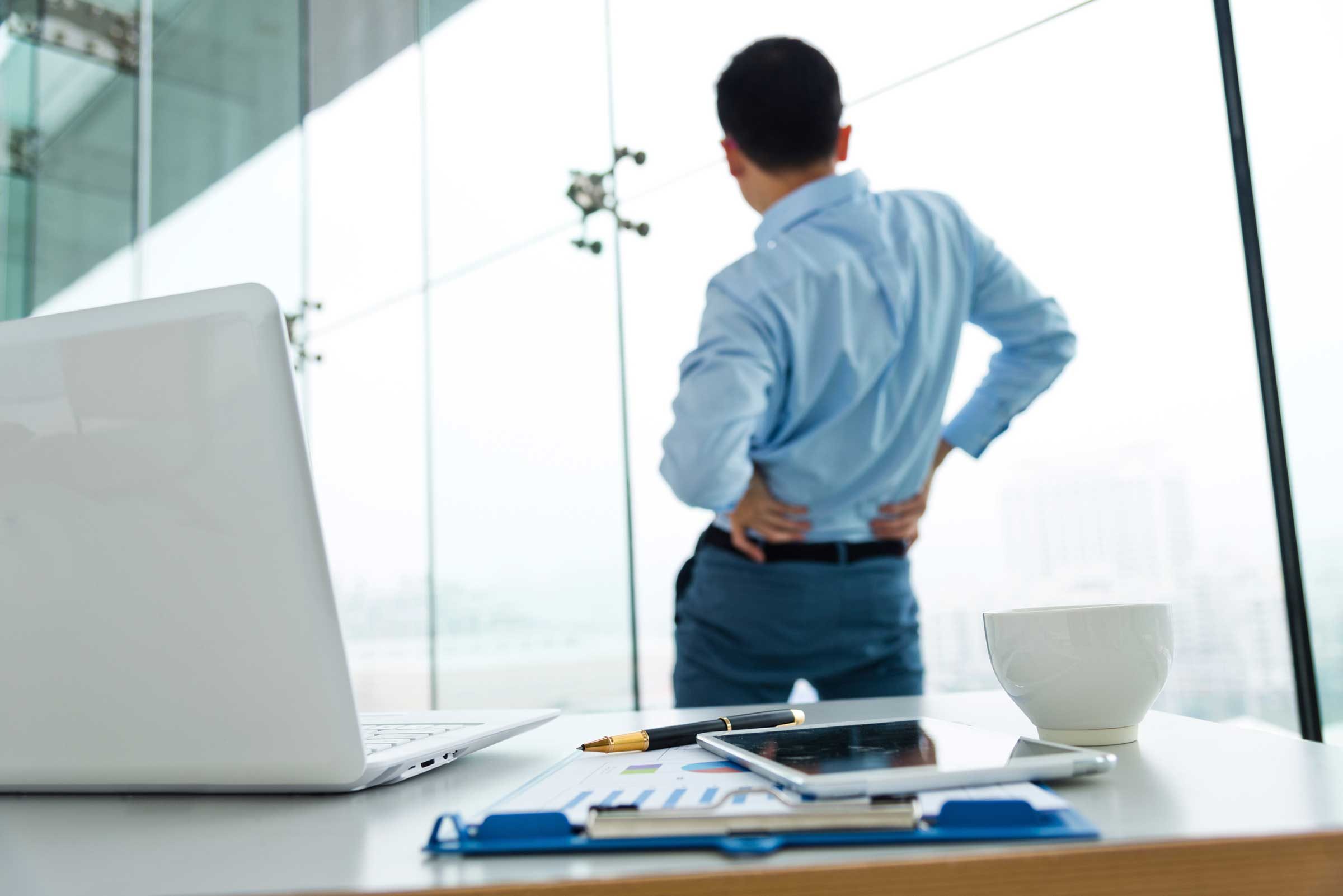 man in office hands on hips and stretching