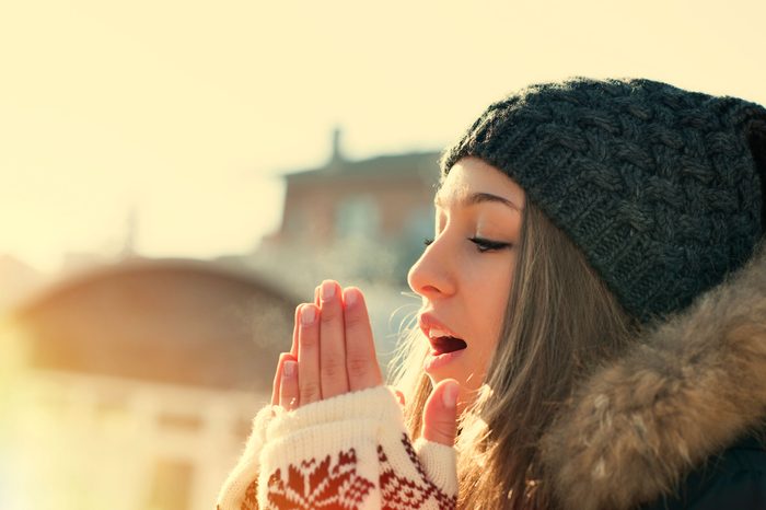 Woman in a beanie blowing onto her gloved hands.