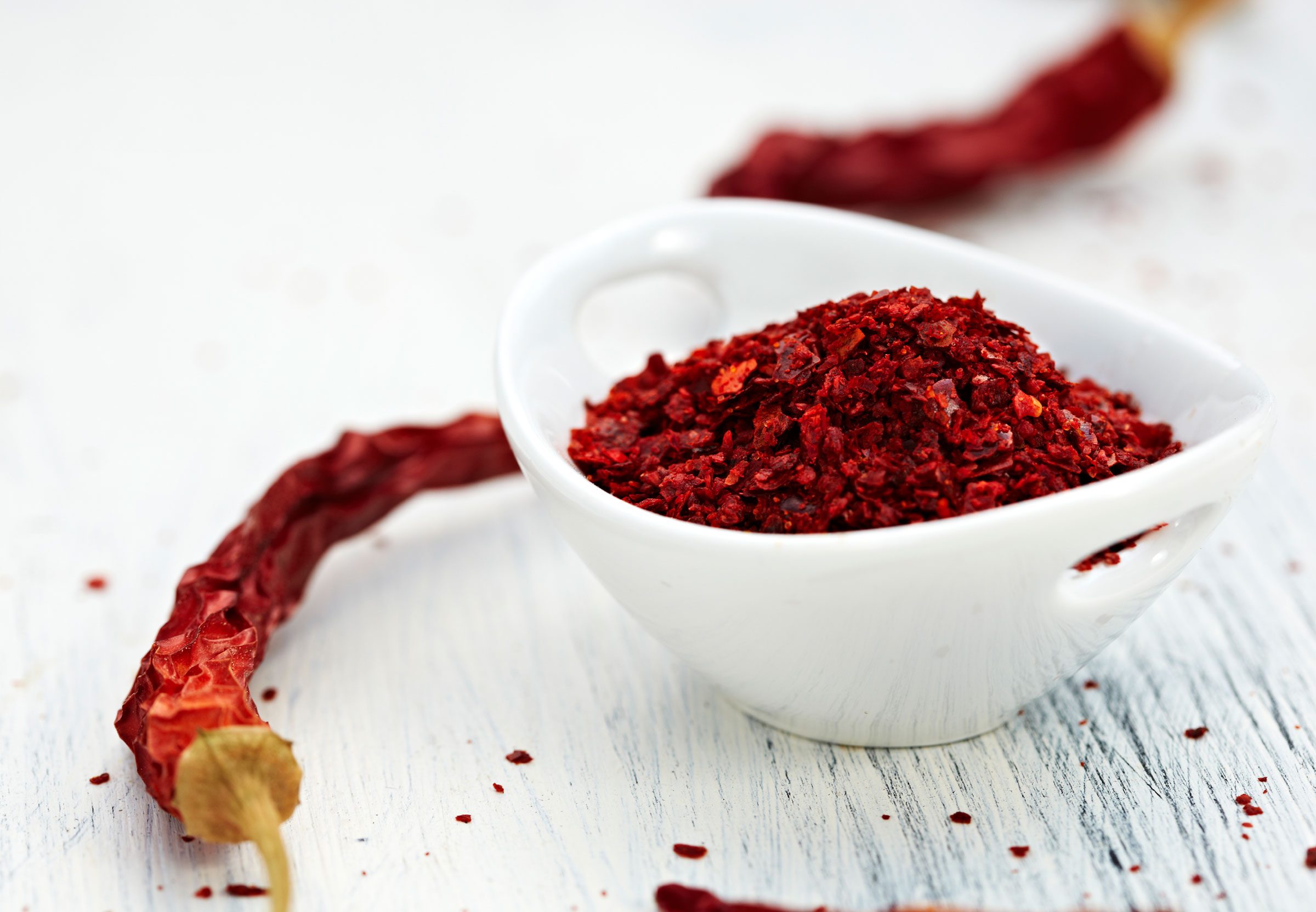 cayenne pepper flakes in a bowl surrounded by whole dried peppers
