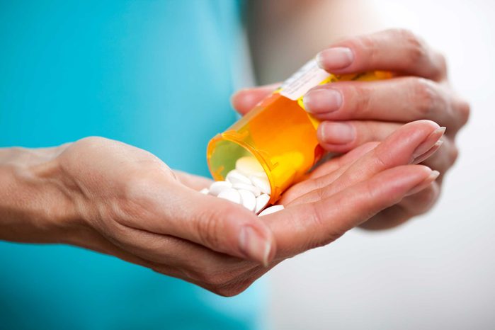 person holding pill bottle and pills