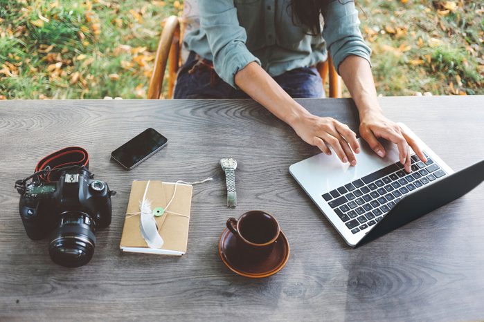 woman working on laptop outside with journal, camera and phone
