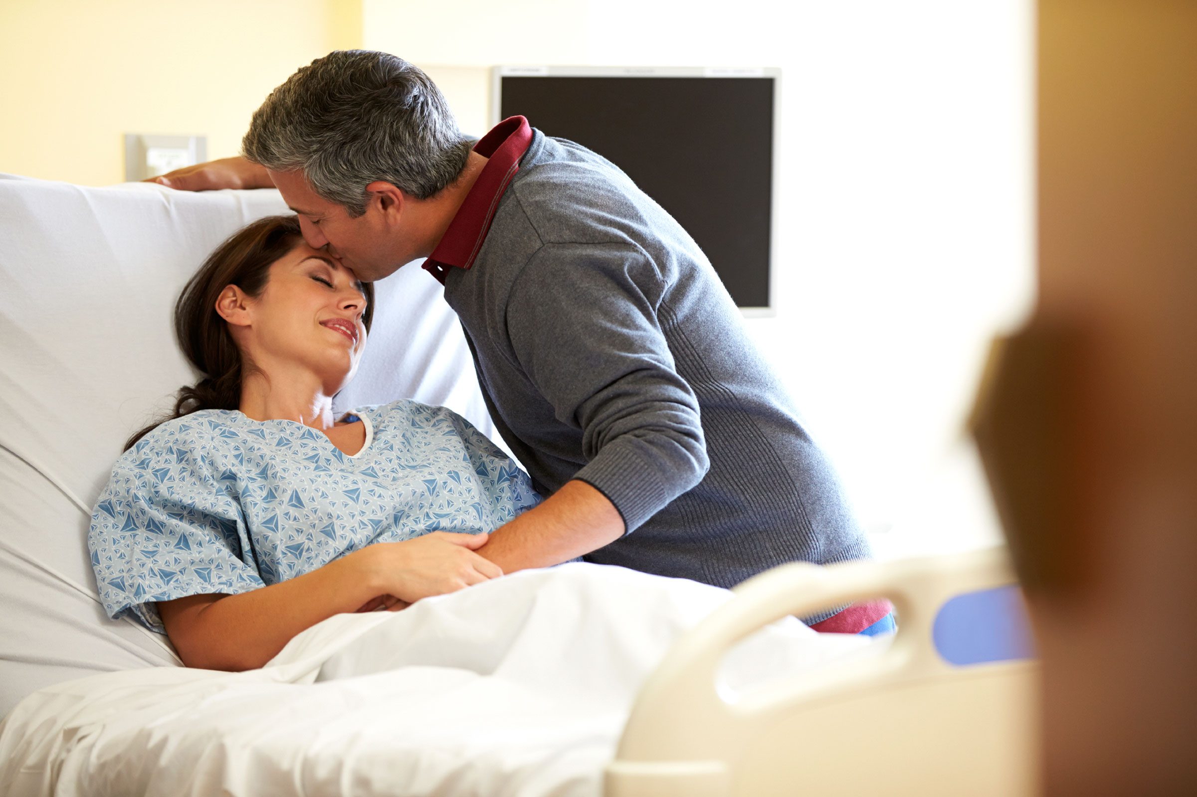 husband kissing his wife who is in a hospital gown in bed