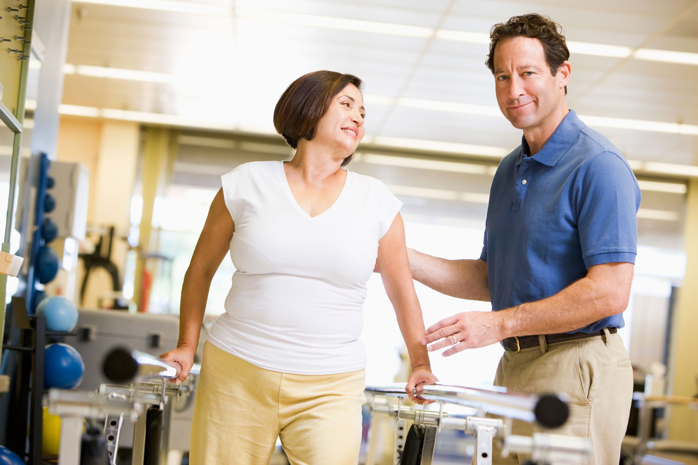 physical therapist helping a woman walk using handrails