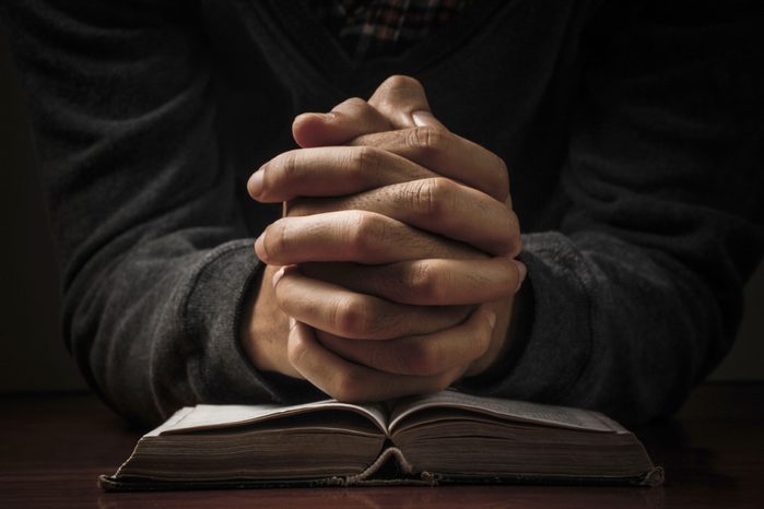 hands folded in prayer over bible