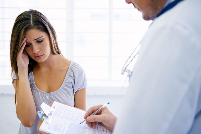 Woman patient holding her head and looking distressed as she talks to a doctor