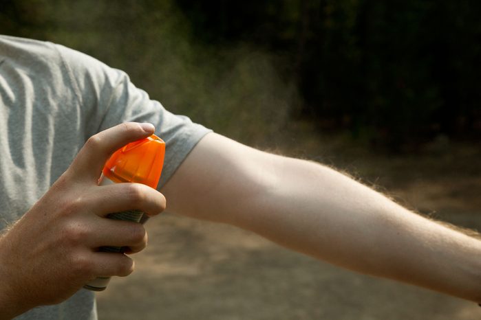 person spraying bug spray on arm