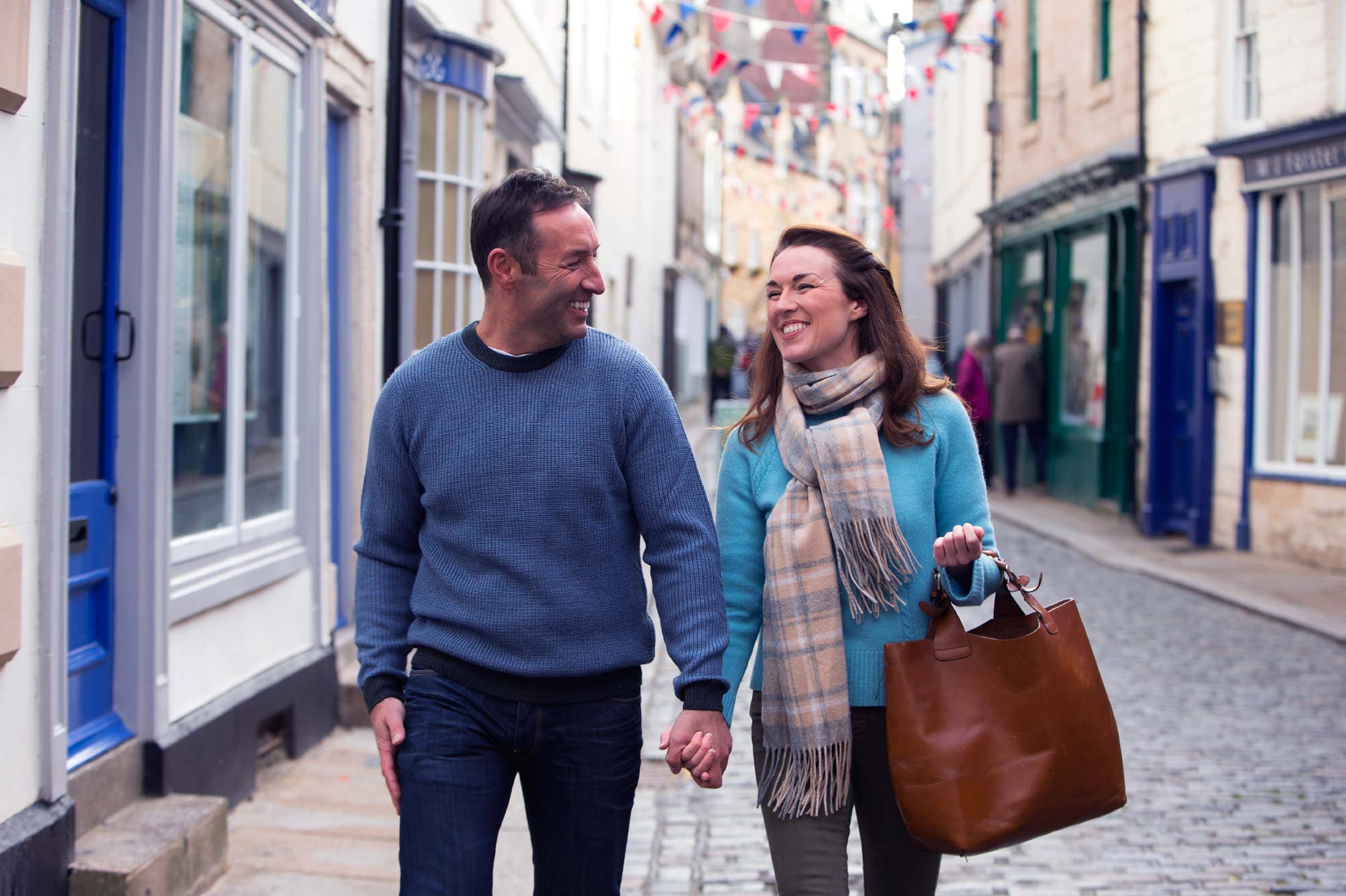 couple holding hands and smiling at each other on cobblestone street