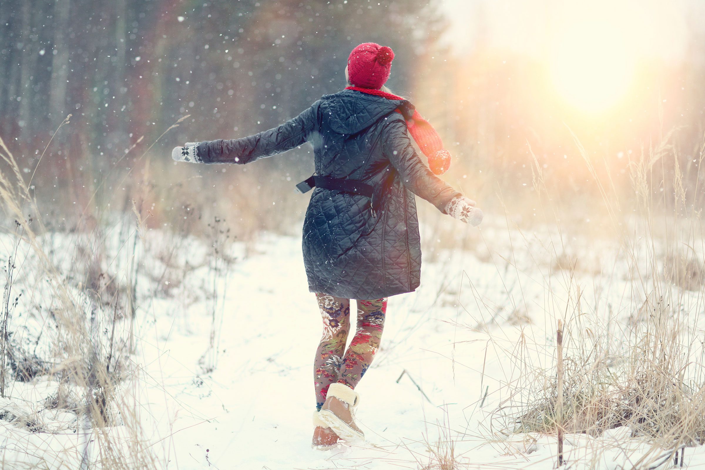 woman in coat and hat walking in a snowy field