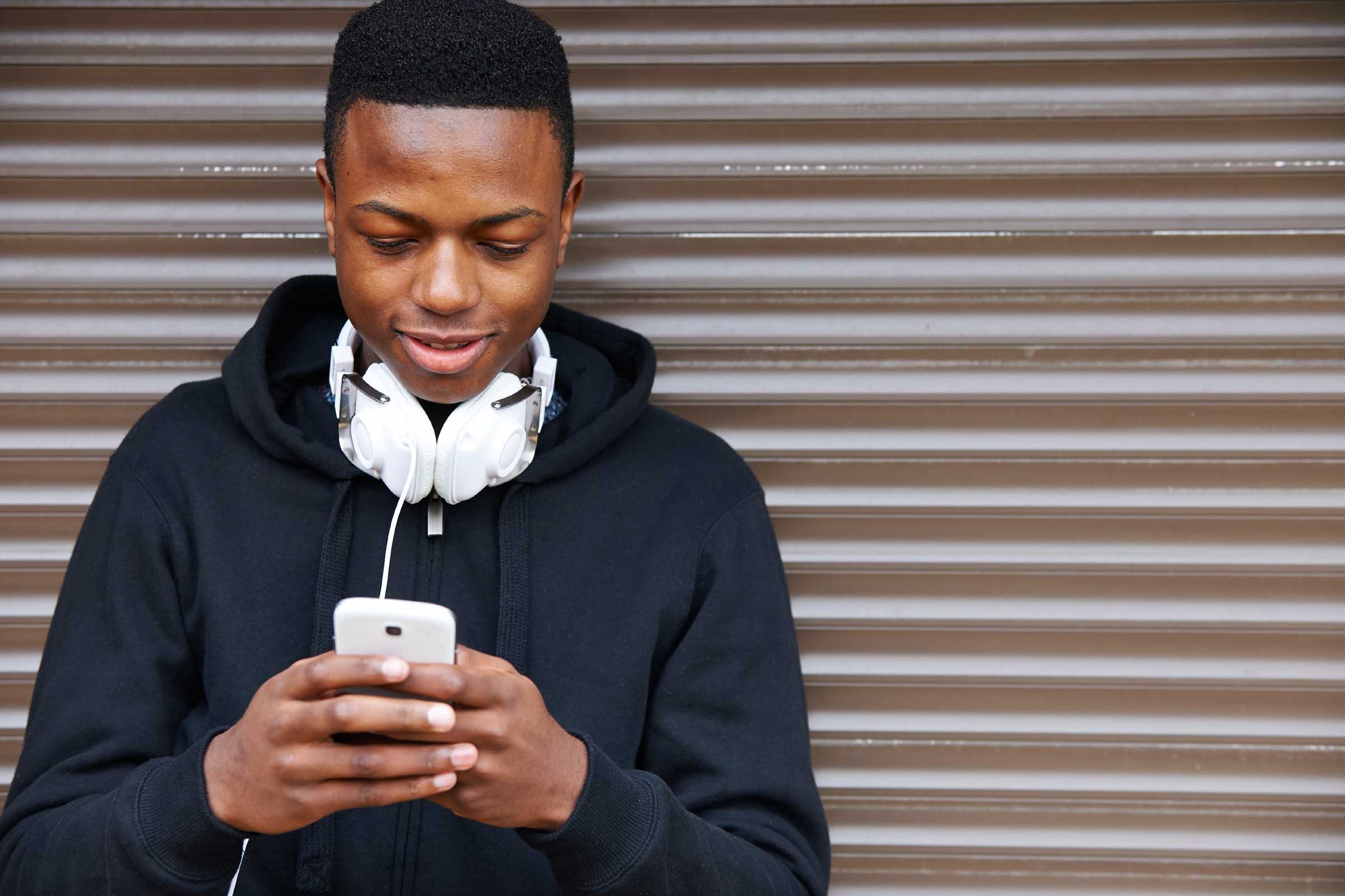 man texting on smartphone, headphones around neck