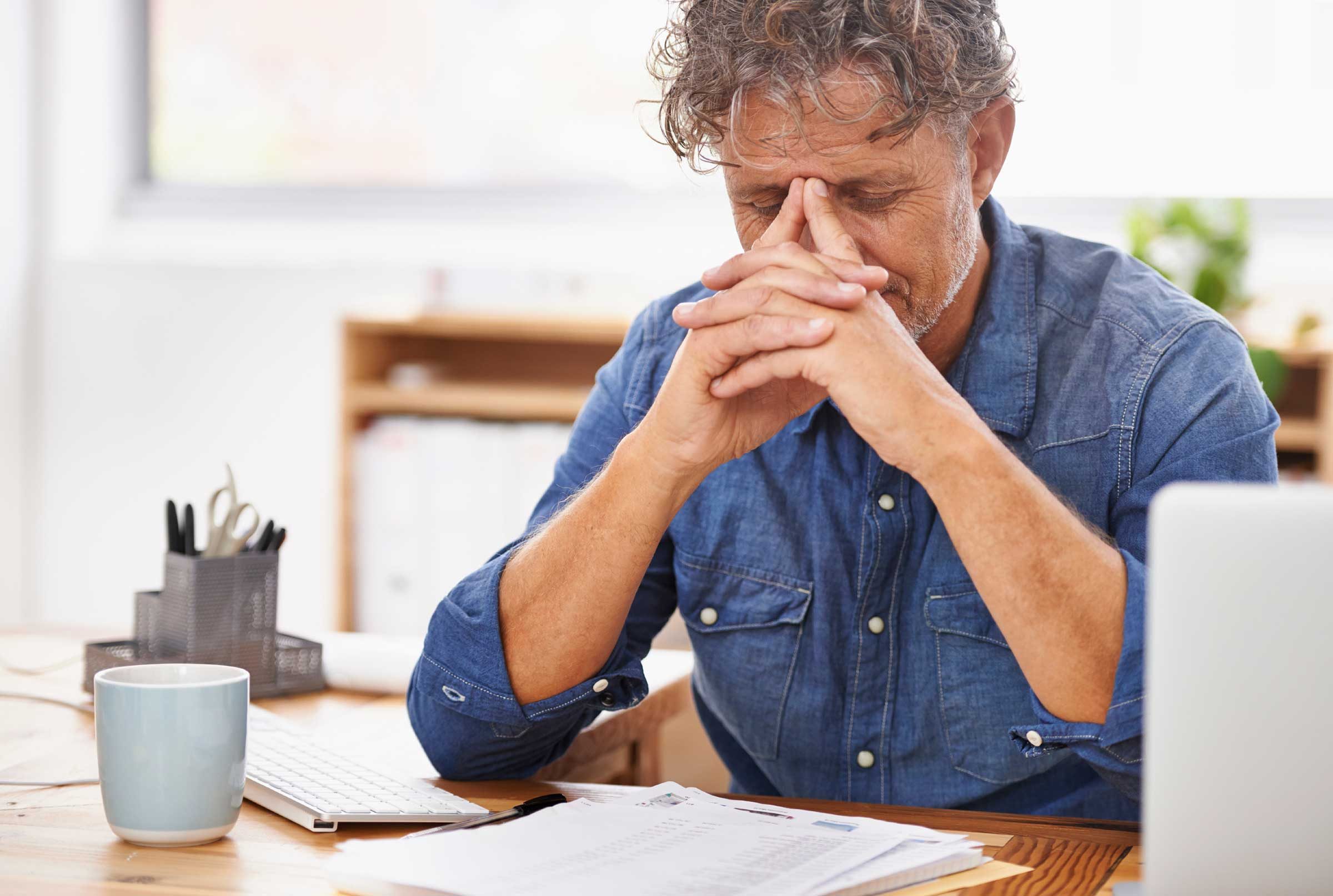 man at desk with computer and work, fingers on head