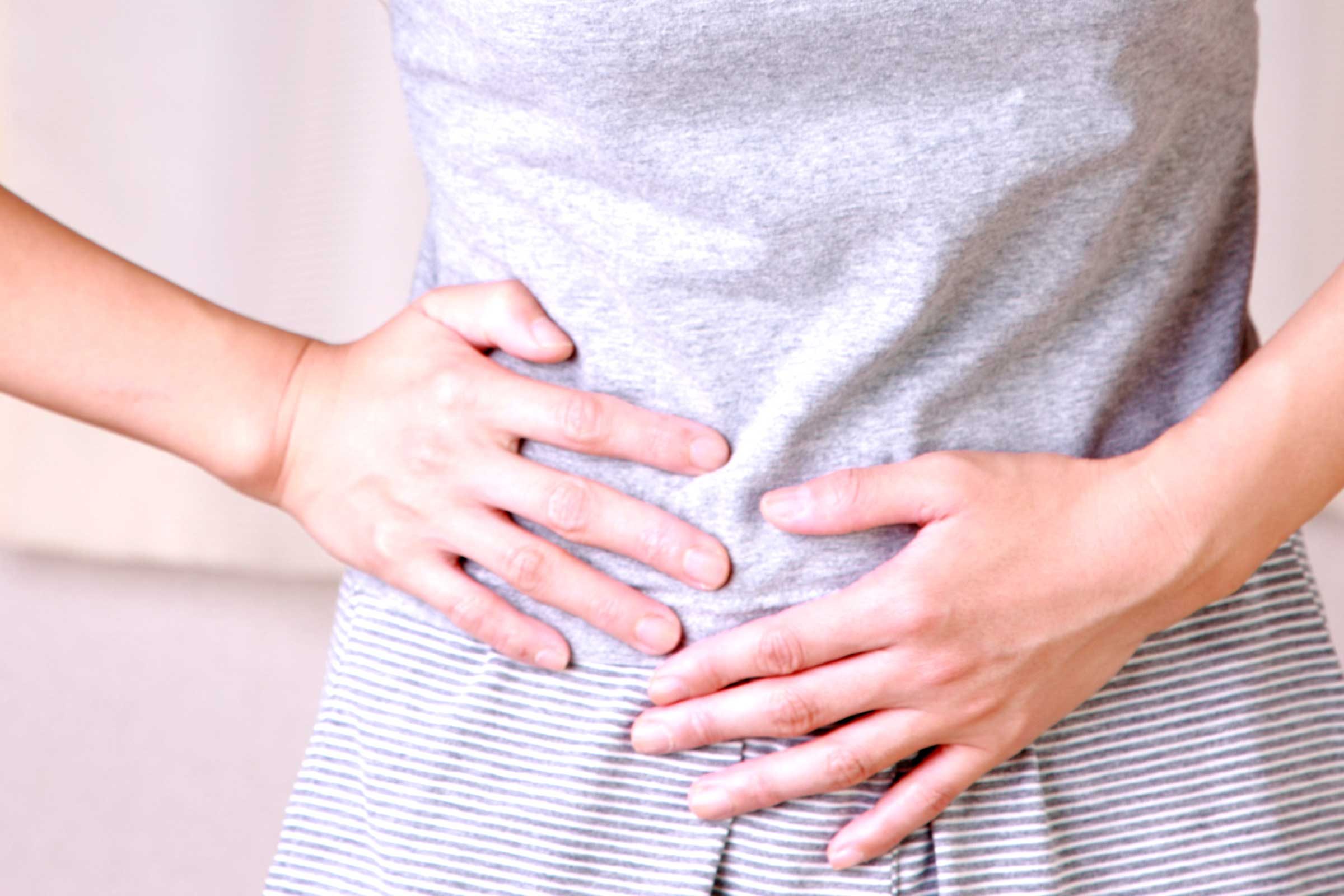 closeup of a woman's abdomen as she clutches her side in pain