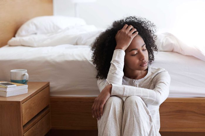 black woman sitting on the floor and leaning against her bed with her eyes closed