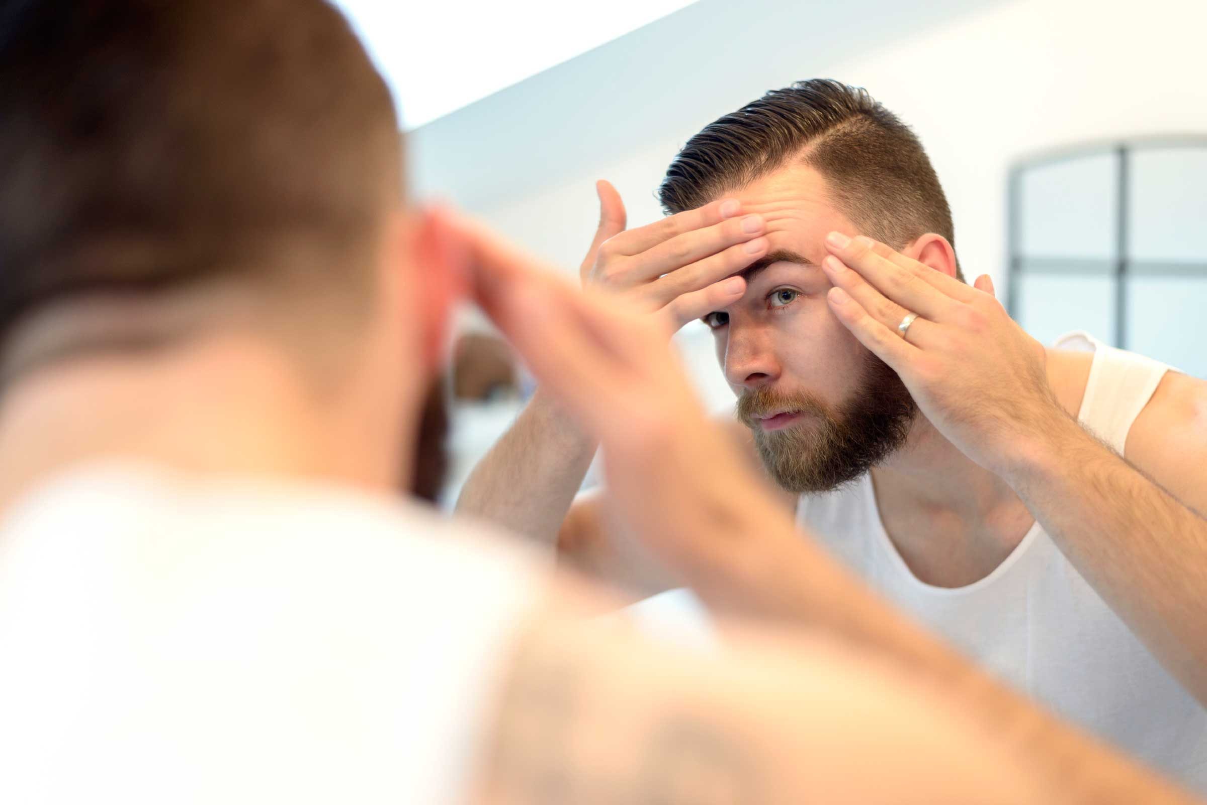 Man checking her forehead for acne in the mirror.