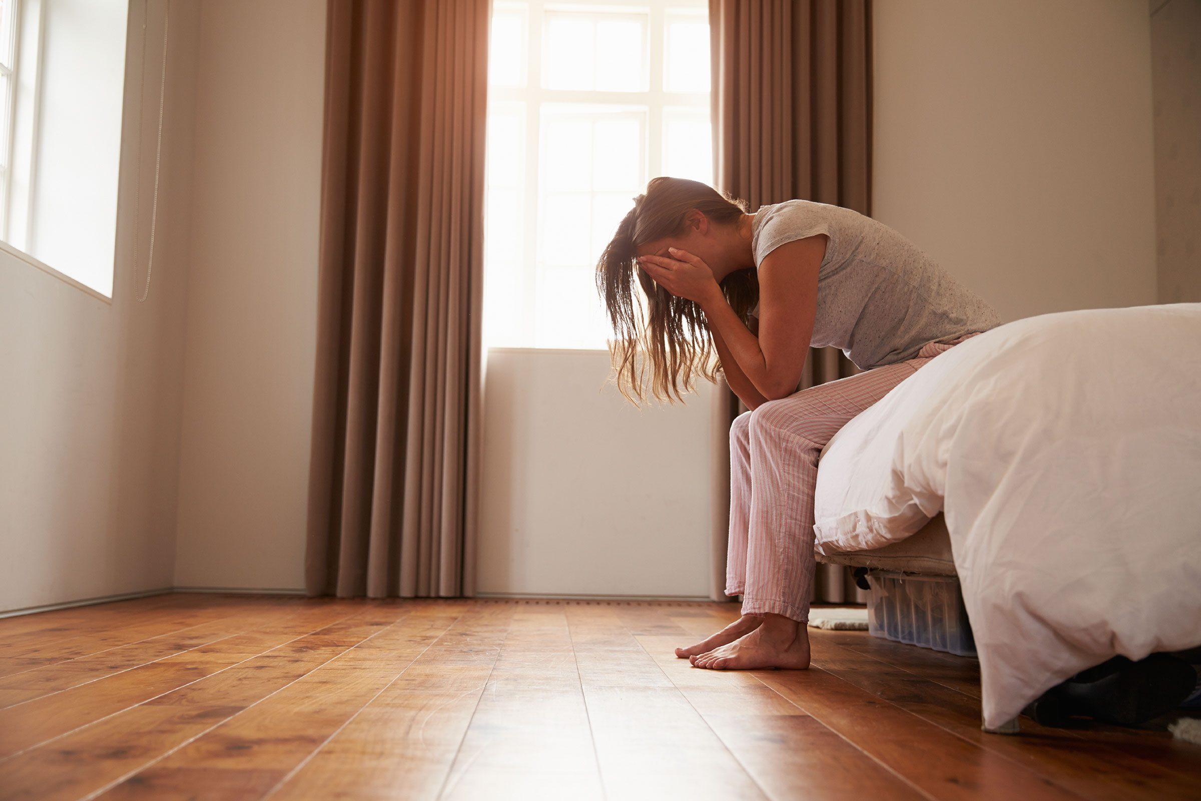 sad woman sitting on bed with head in hands