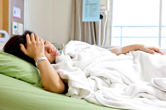 woman in hospital bed, hand on forehead