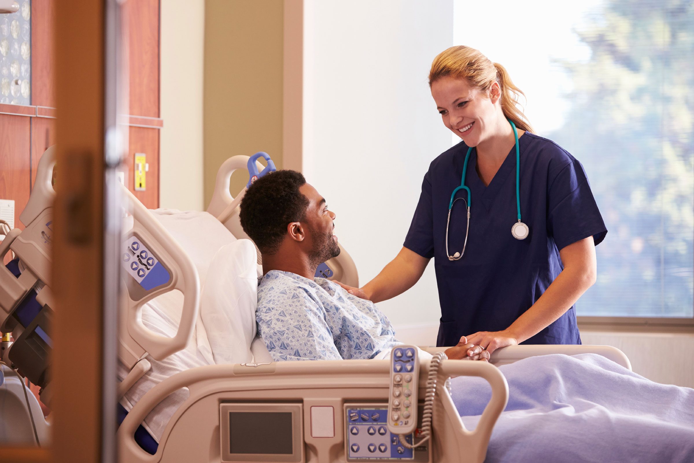 woman with stethoscope talking to patient in hospital bed