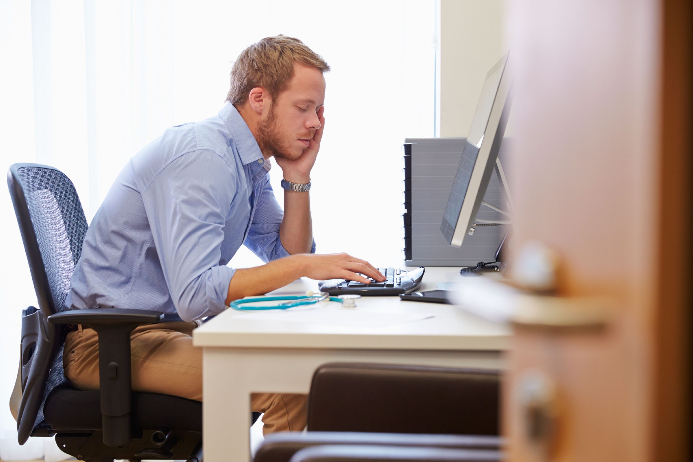 unhappy man at desk with computer and stethoscope
