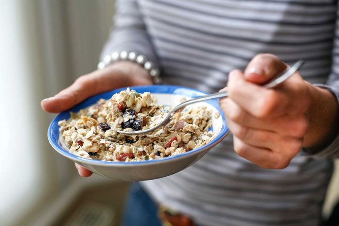 woman with bowl of cereal with berries, taking a spoonful