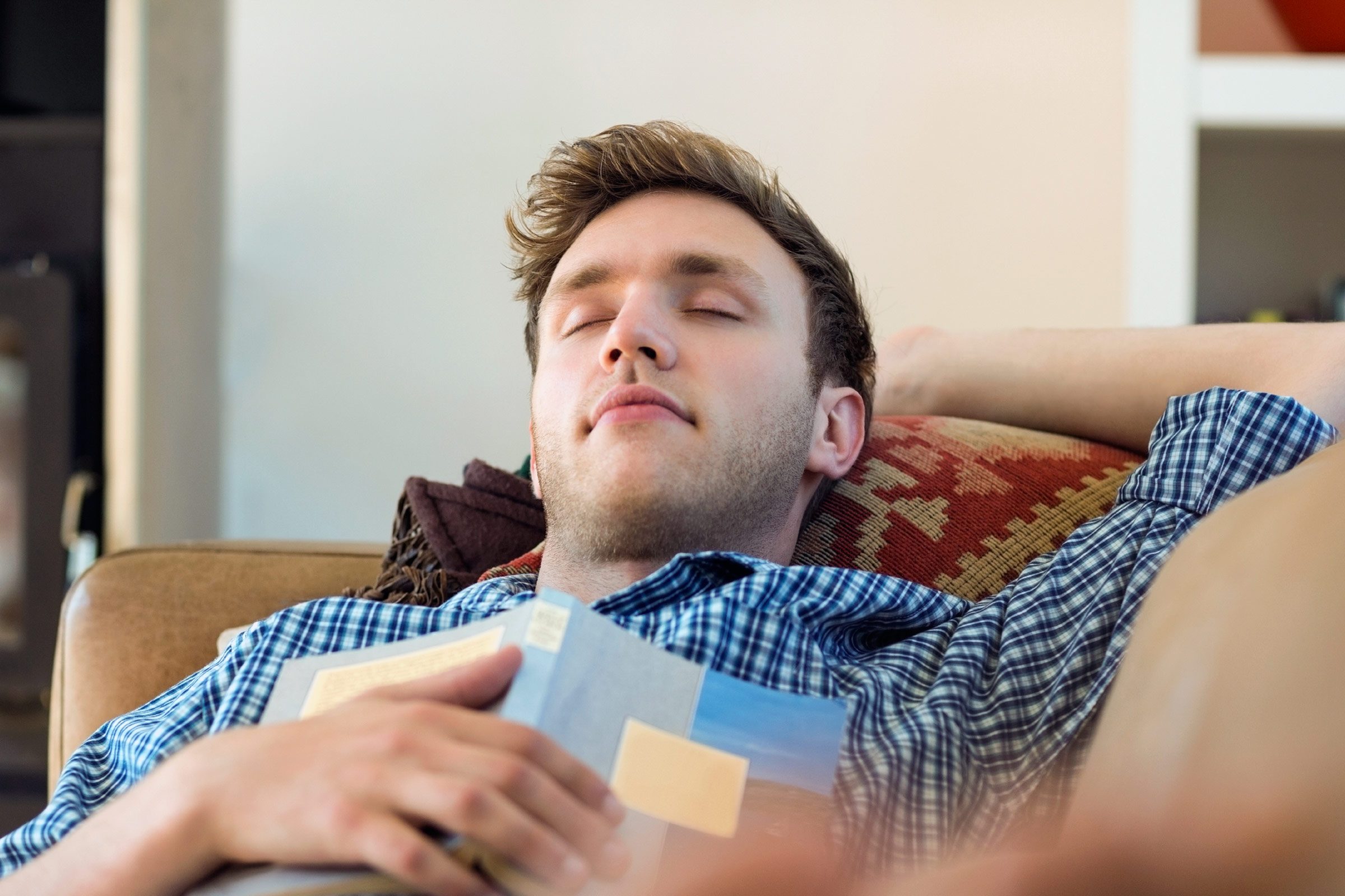 man asleep on his back on a couch, book on his chest