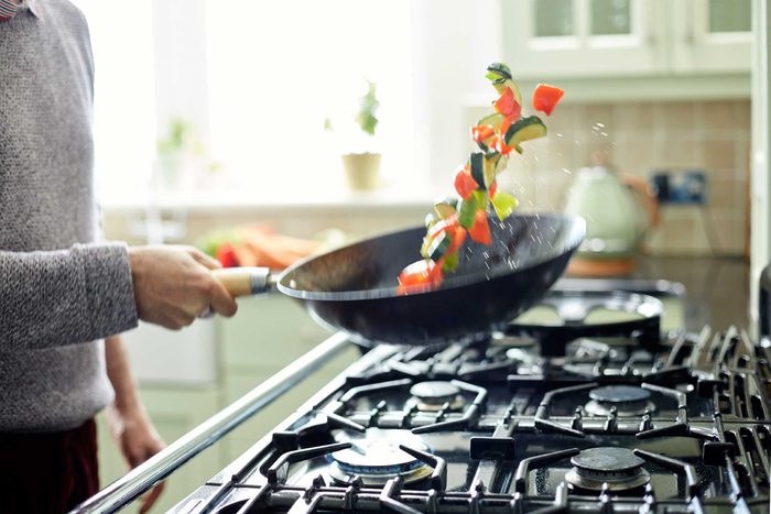 person sauteeing vegetables in a pan over oven
