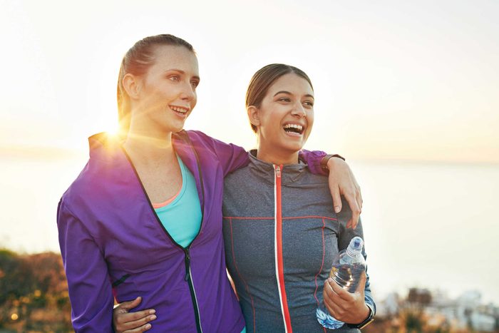 two smiling women in workout clothes, arms around each other, outside
