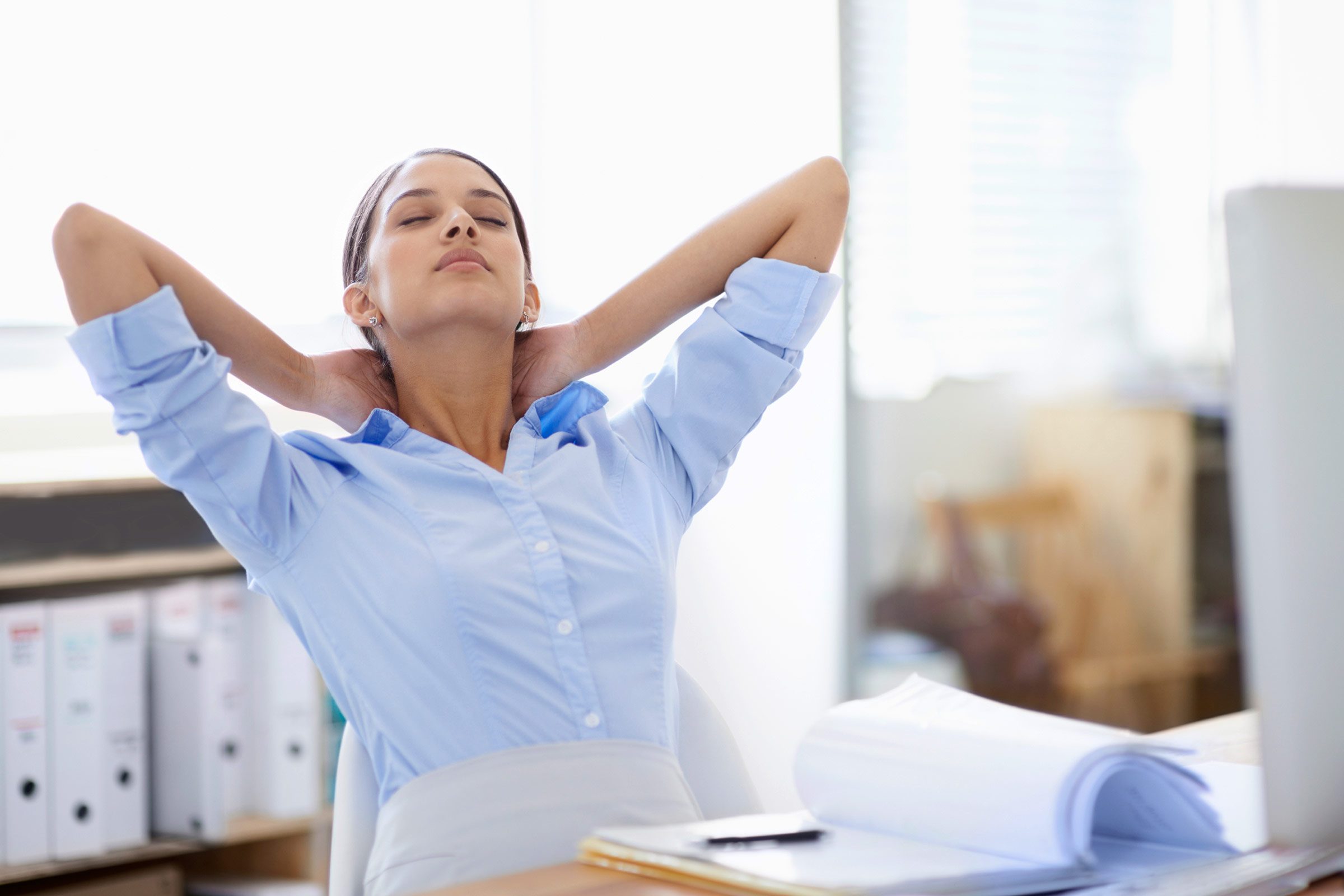 professional woman leaning back in a chair with her hands behind her neck, eyes closed