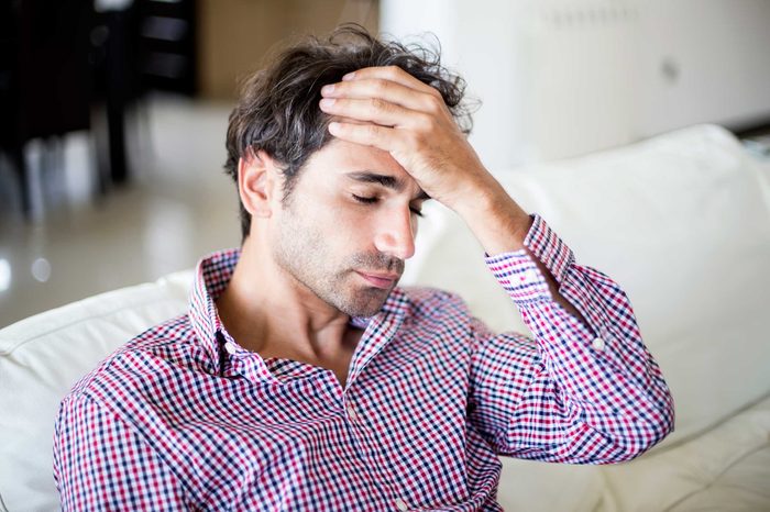 Man sitting on a couch holding his forehead with one hand.