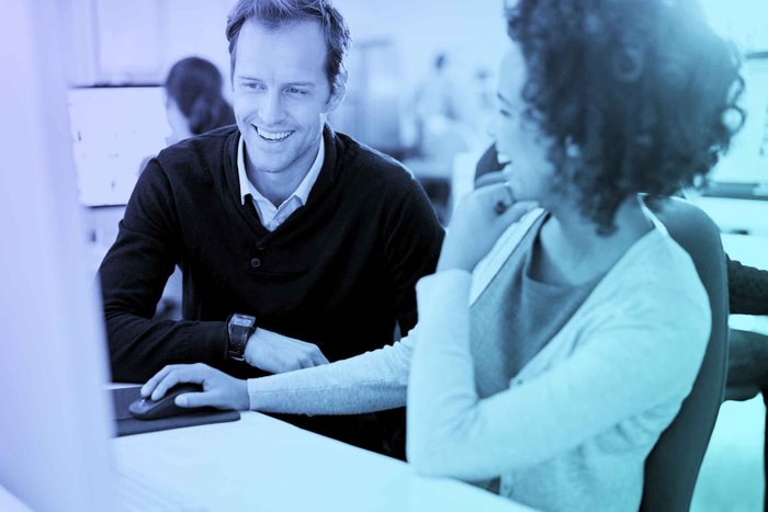 man and woman in an office setting, talking next to a computer