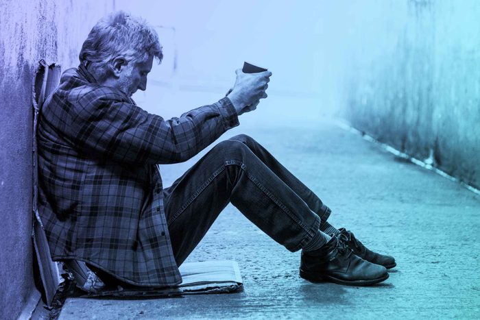 homeless man in an alley holding a donation cup