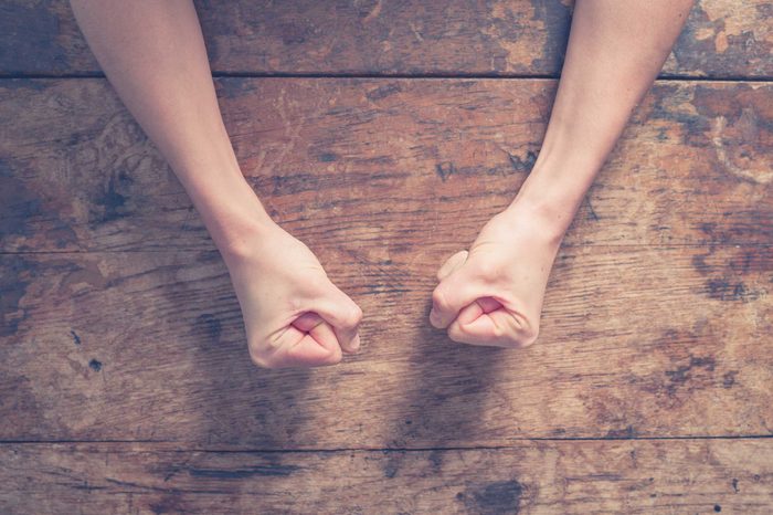 Person's clenched fists on a wooden table.