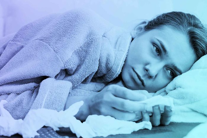 woman wearing a robe and holding tissues, in bed