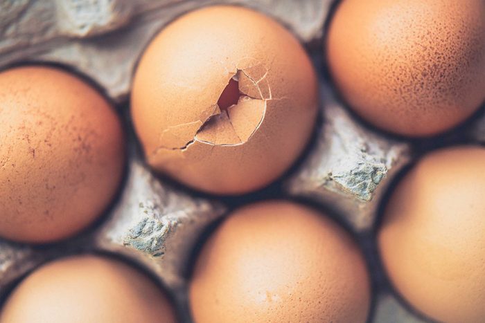 brown eggs in a carton, one is cracked