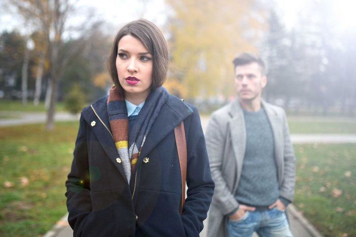 Woman in a coat walking in a park in front of a man.