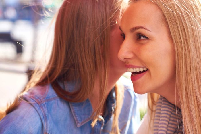 A woman whispering in another woman's ear.