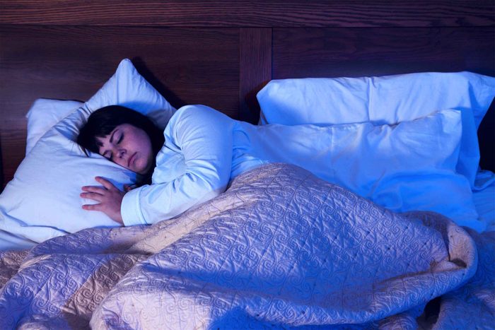 woman in cozy bed in dark room with pillows