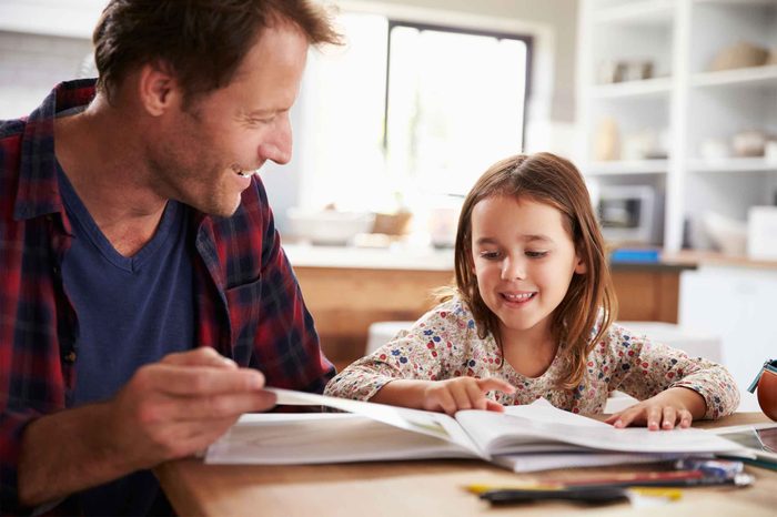 Father and daughter reading a book at the kitchen table.