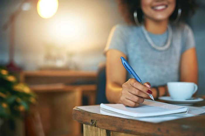 Woman sitting at a table writing in a notebook with a pen.