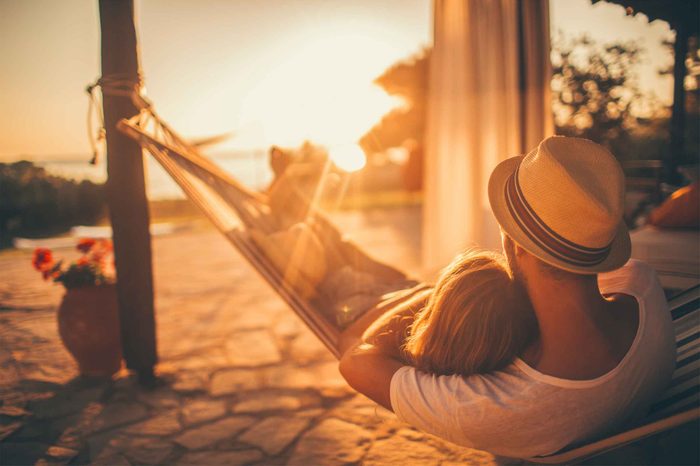 A man and woman lying in a hammock on a patio outdoors.