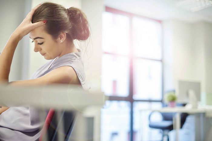 woman sitting in chair, looking down and holding forehead