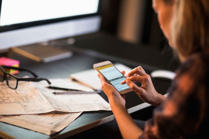 woman sitting at desk typing into smartphone