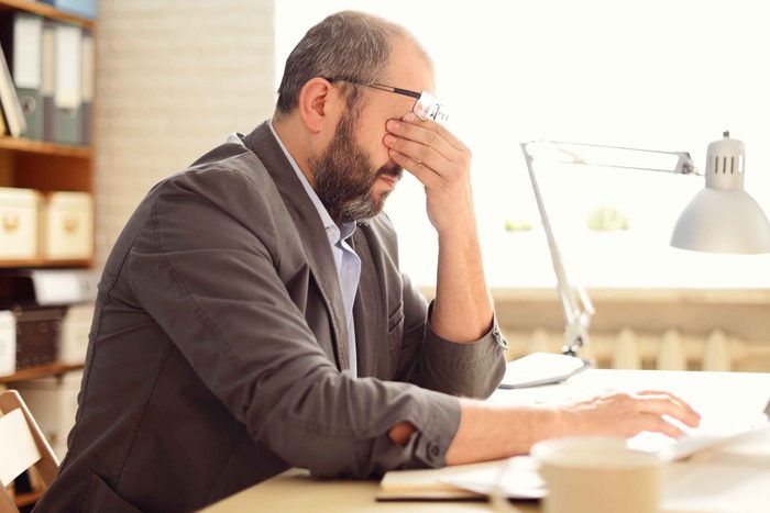 man sitting at a desk in an office rubbing his eyes