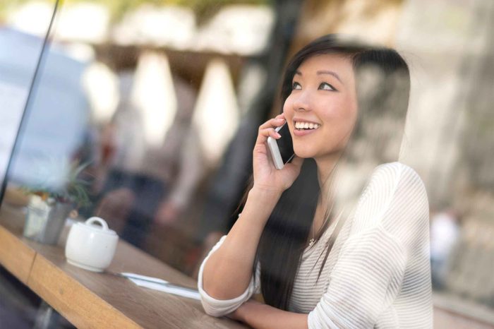 Woman sitting in a coffee shop smiling and talking on her phone.