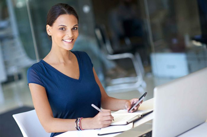 Woman in a blue shirt sitting at a desk writing in a journal.