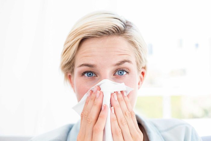 Woman with bright blue eyes blowing her nose.