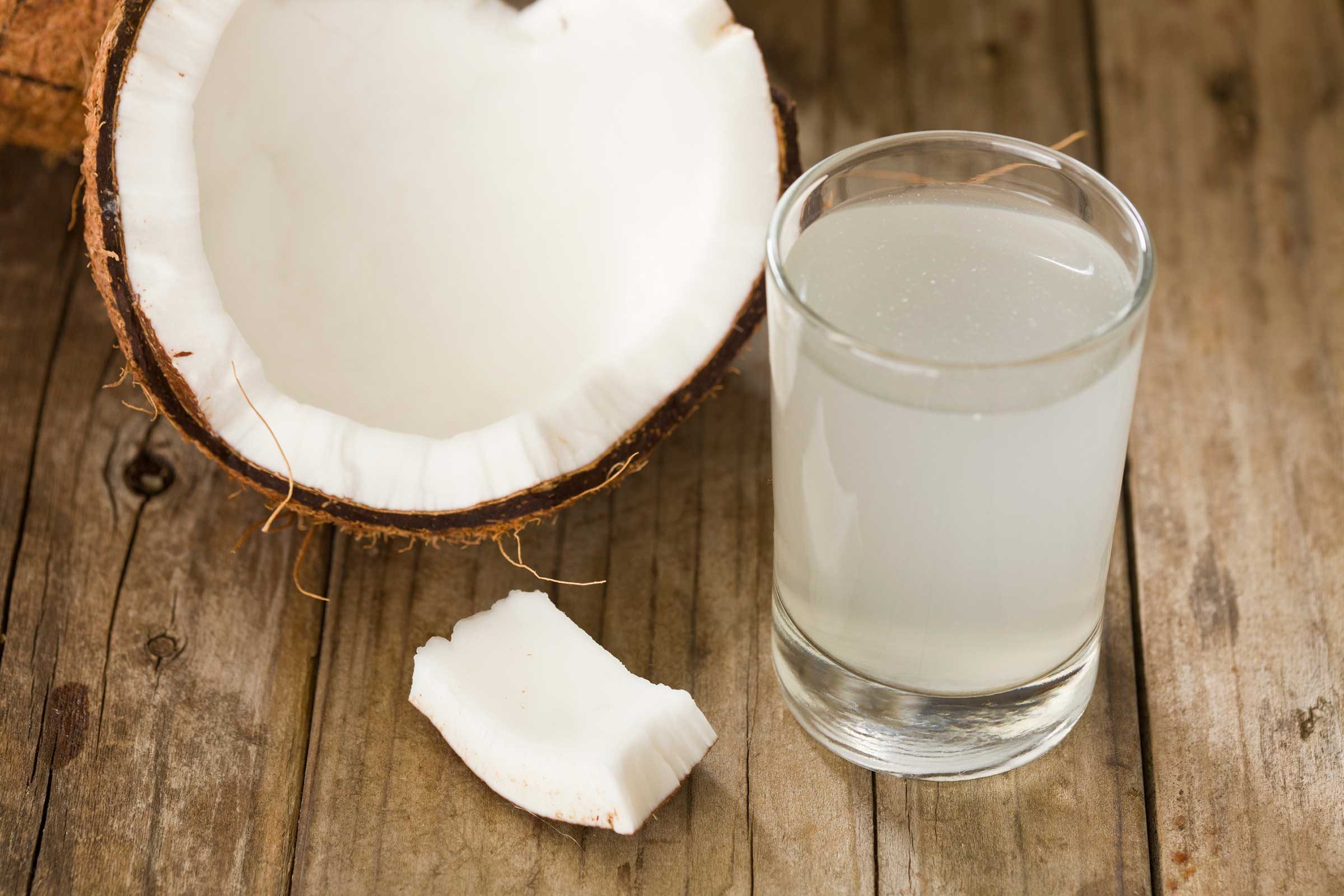 glass of coconut water in front of halved coconut